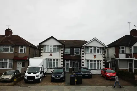 A row of interwar houses with white-painted gables, bay windows and paved front driveways under a grey sky, with a van and cars parked in front