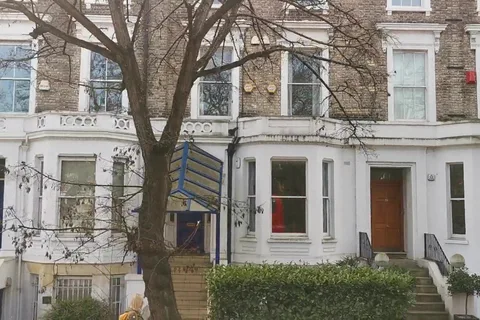 A pair of tall Victorian villas with white stucco ground-floor bay windows, yellow-brick upper floors, steps up to the front doors, a hedge and a bare tree in front